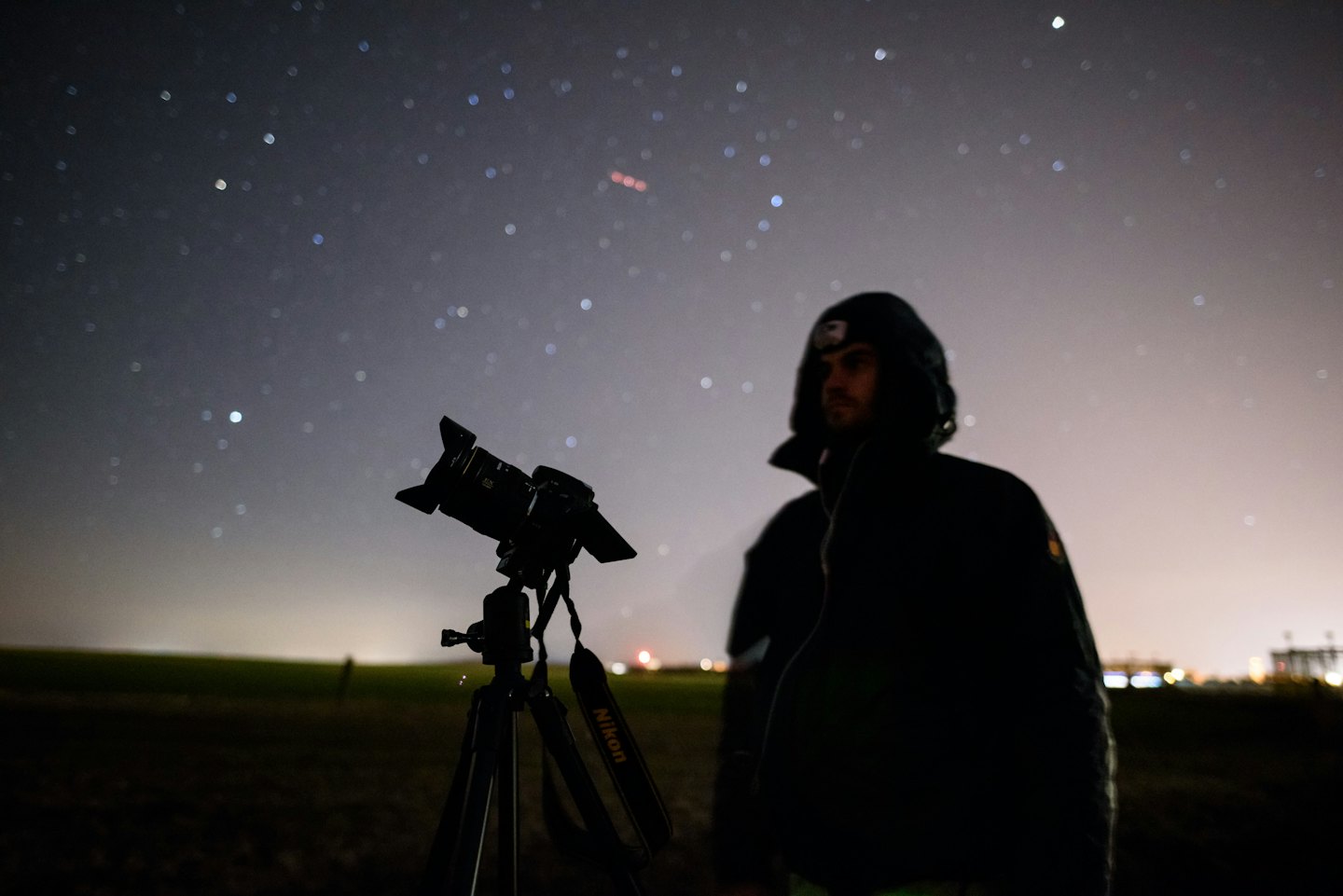 Photographer stands by his tripod looking at the starry night sky.