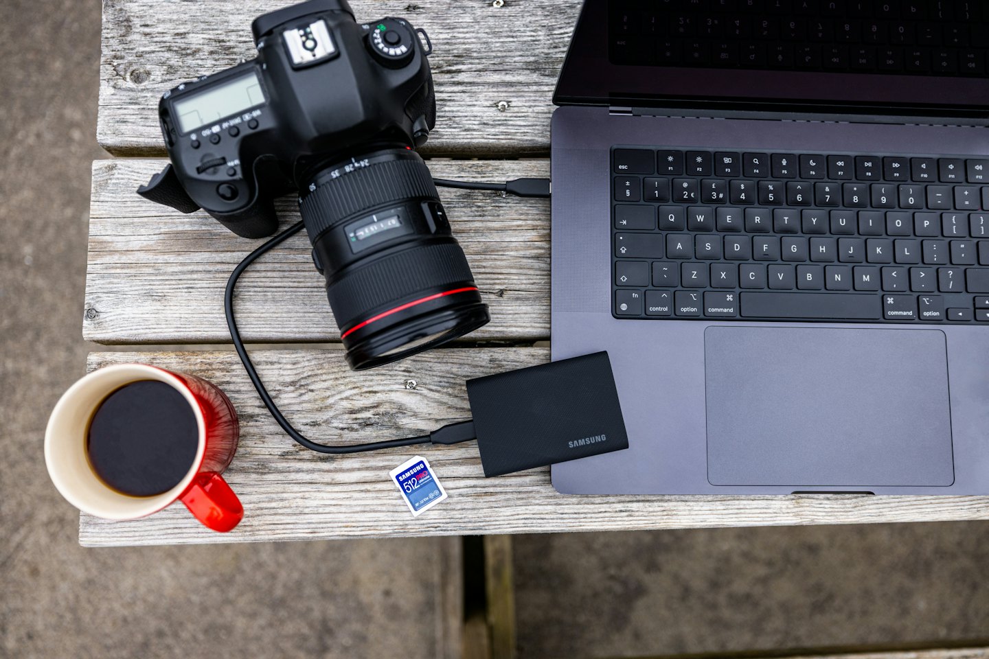 Camera gear and laptop setup on a wooden picnic table.