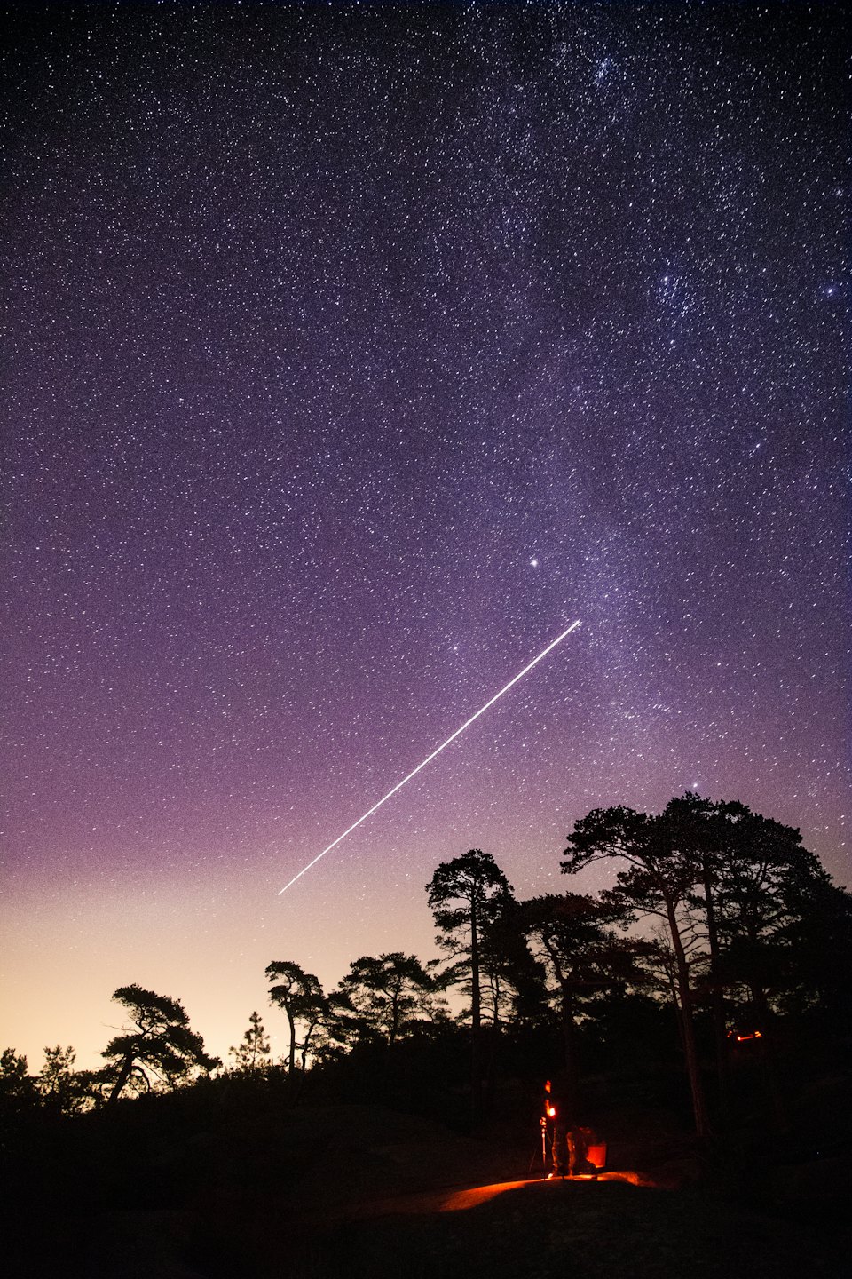 Person setting up camera equipment under starry night sky.